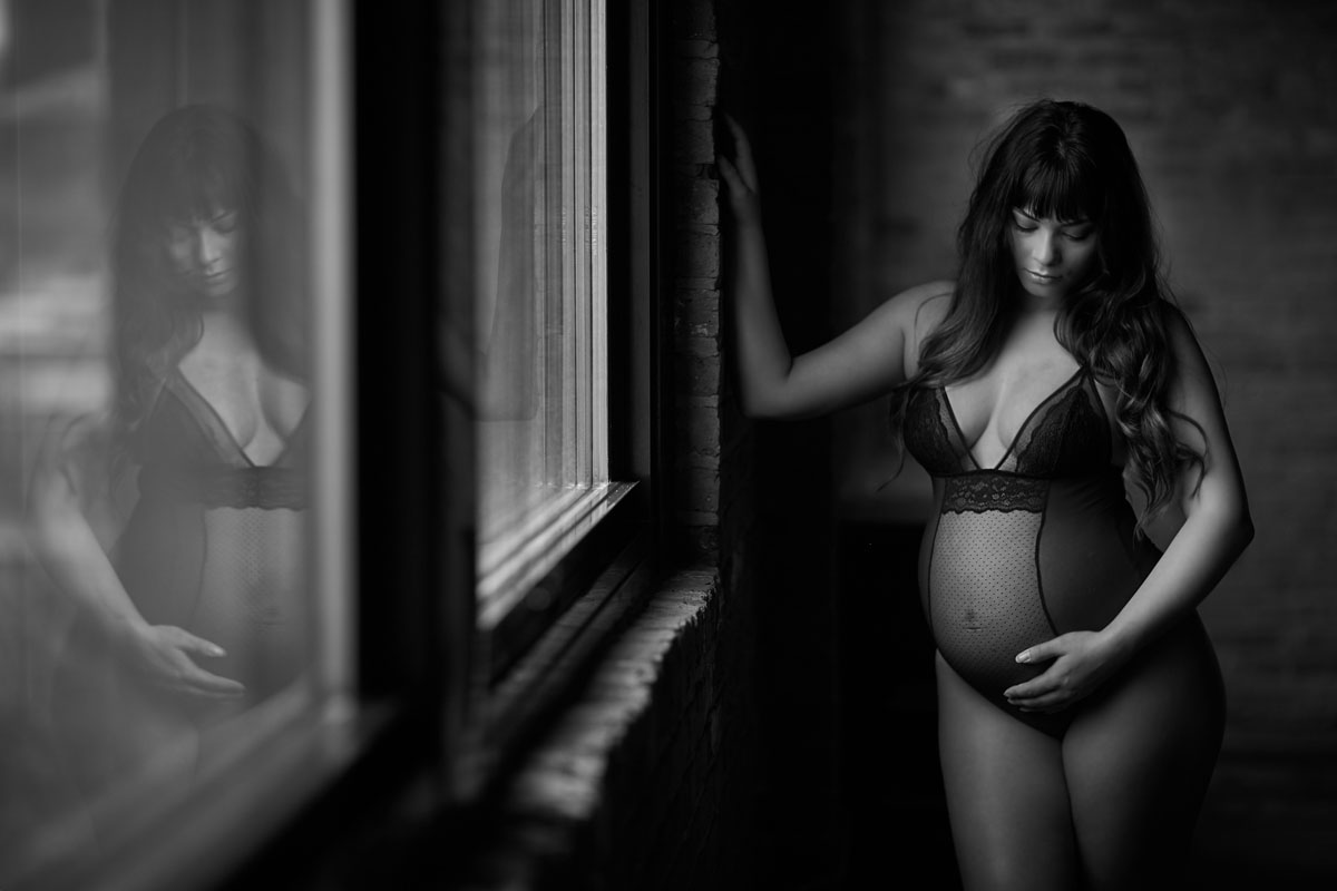 pregnant woman standing next to window maternity boudoir black and gray